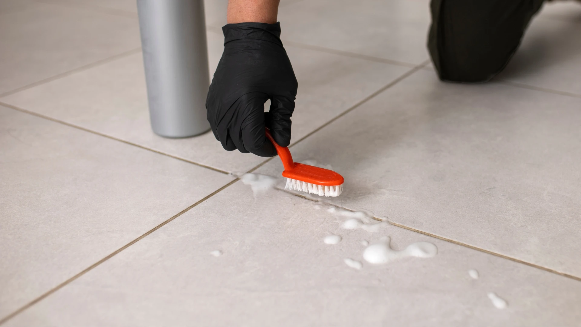 Gloved hand scrubbing tiled flooring and grout lines